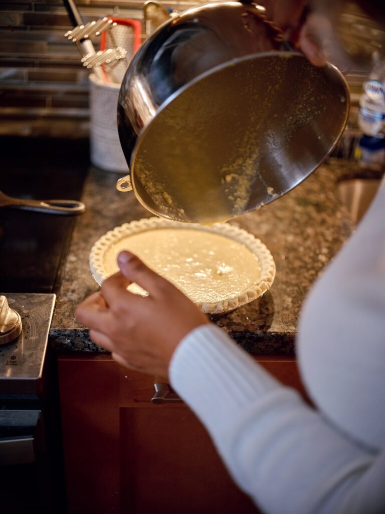 Hands pour pie filling out of metal bowl into pie crust.