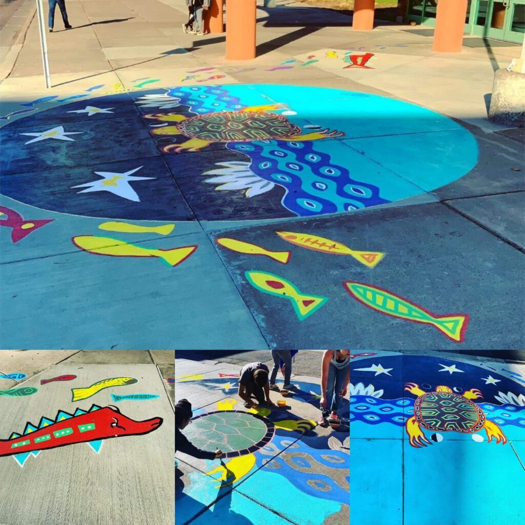 Circular mural painted on sidewalk with waves, stars, turtle, and fish.