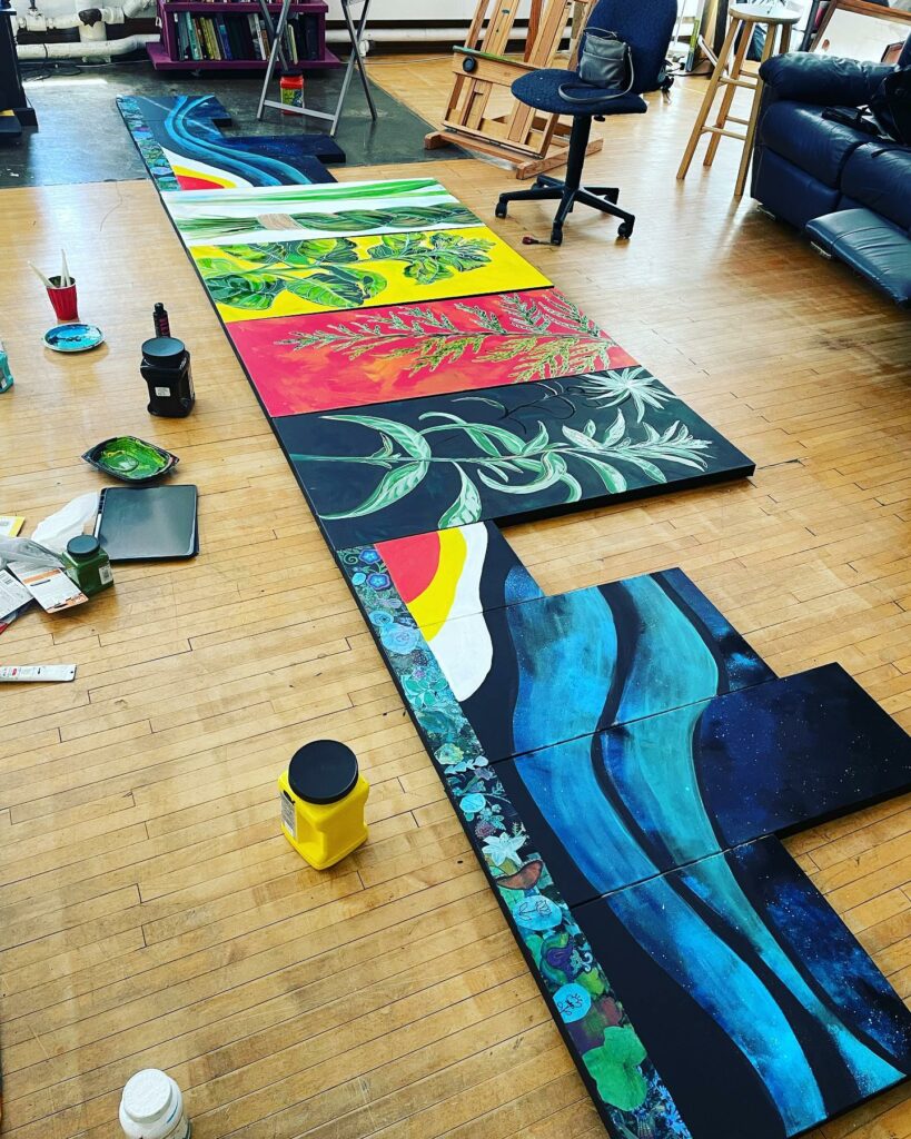 Painting with many panels laid out on wood floor in studio.