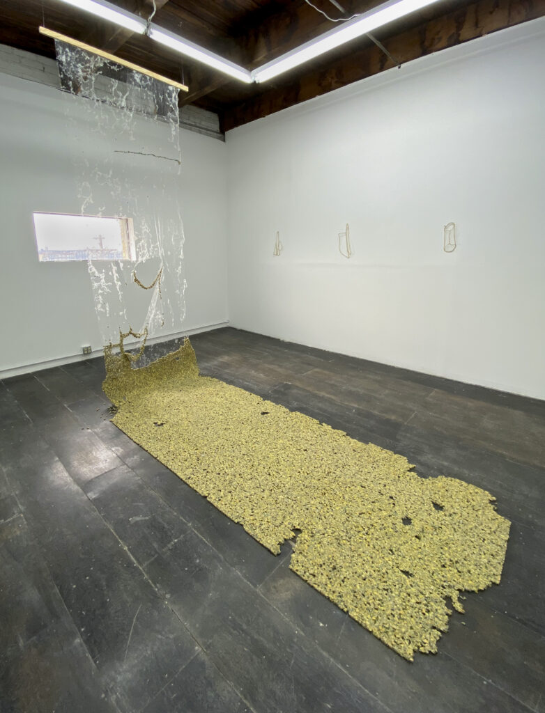 Gallery installation of sculpture made from yellow furniture padding, suspended in tatters from ceiling and flat on floor.