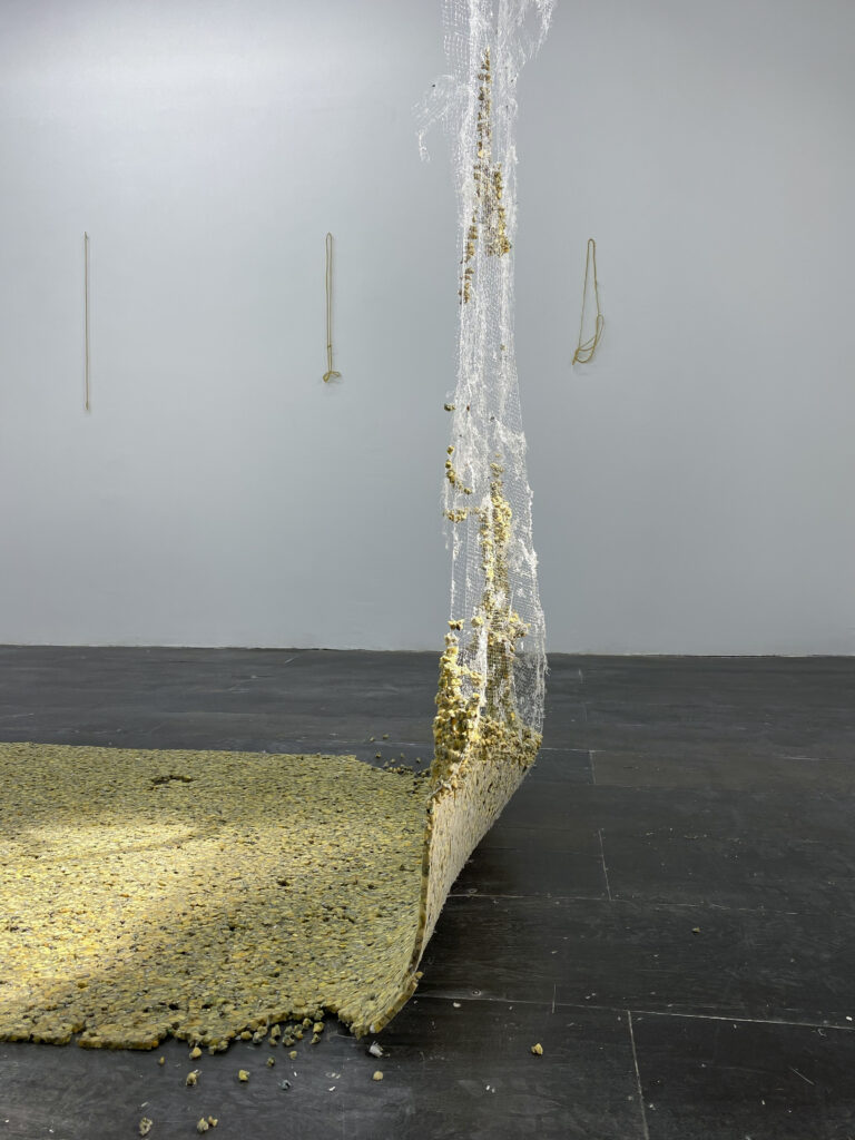 Gallery installation of sculpture made from yellow furniture padding, suspended in tatters from ceiling and flat on floor.
