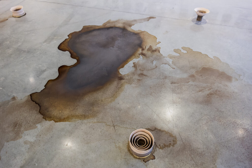 Pool of dried brown liquid on smooth gray floor with three small round sculptures.