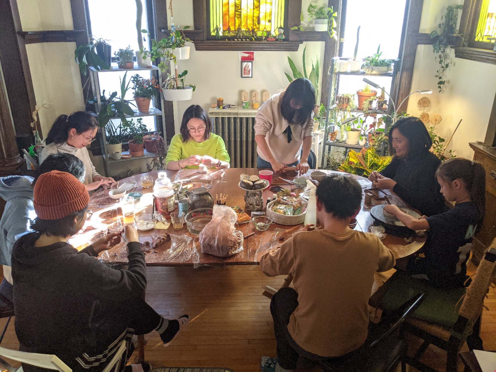 Group of people sit around dining room table, working with clay.