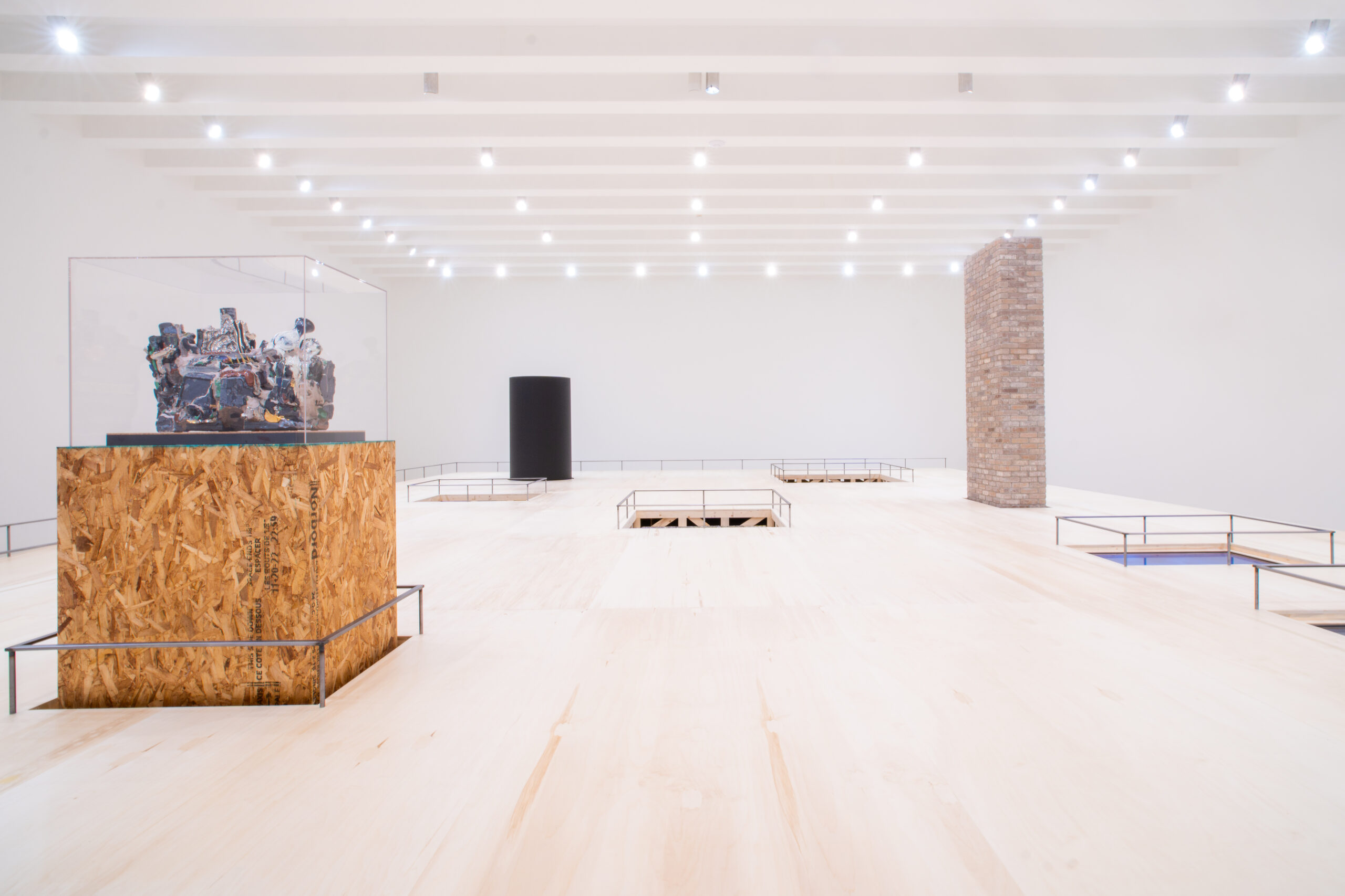 Gallery with white walls, white ceiling, and light wood flooring with several sculptures, some recessed into the floor.