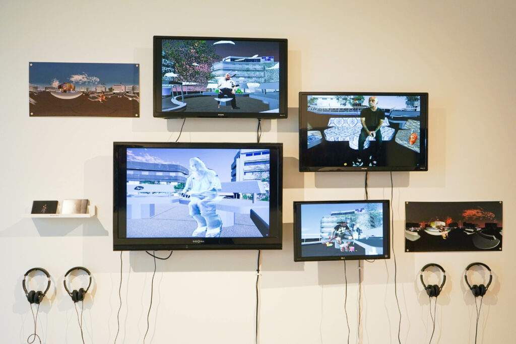 Many video monitors with headphones installed on white gallery wall, all with different images of human figures in front of urban landscapes.