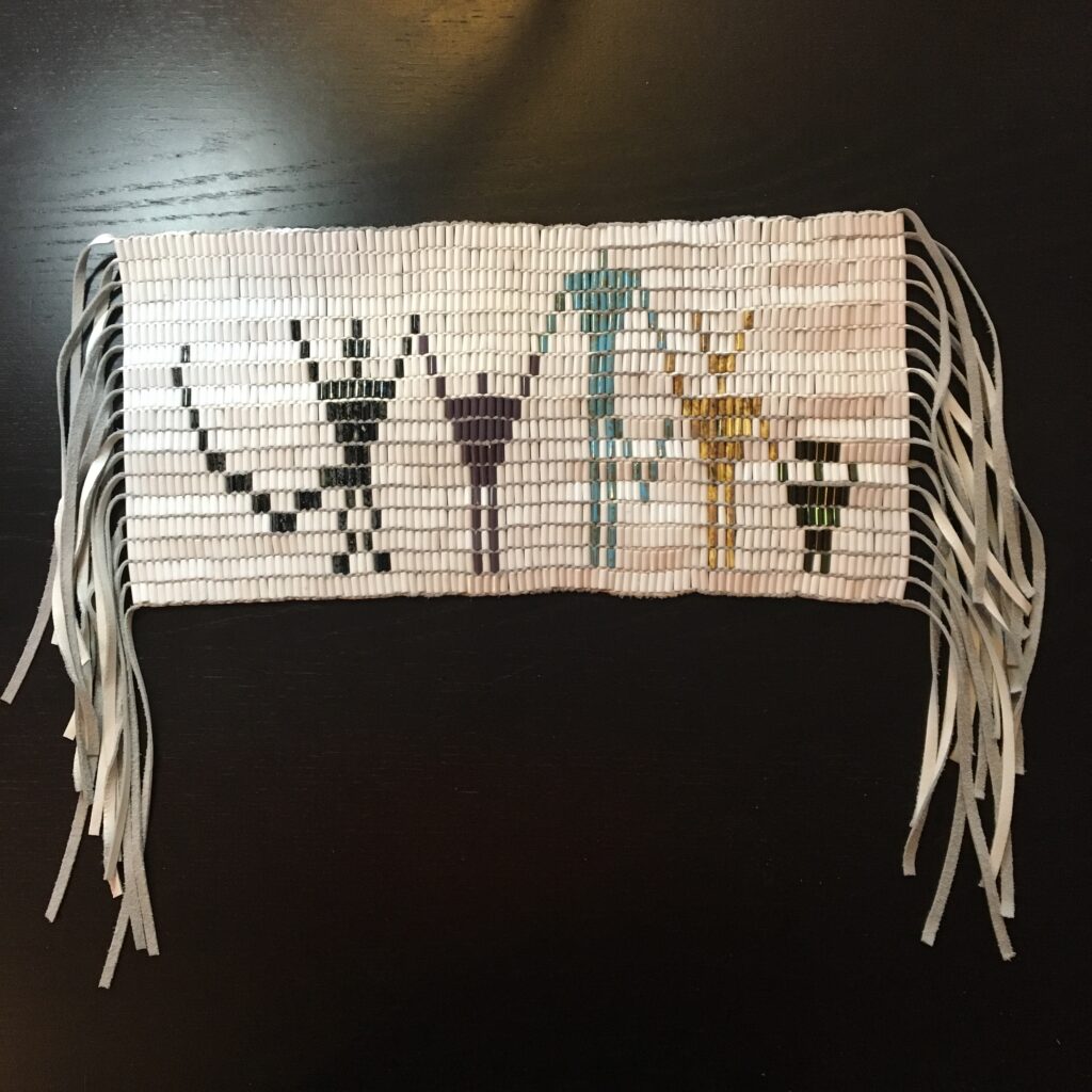 Wampum belt with beaded pattern depicting five figures, and leather fringe on both sides.