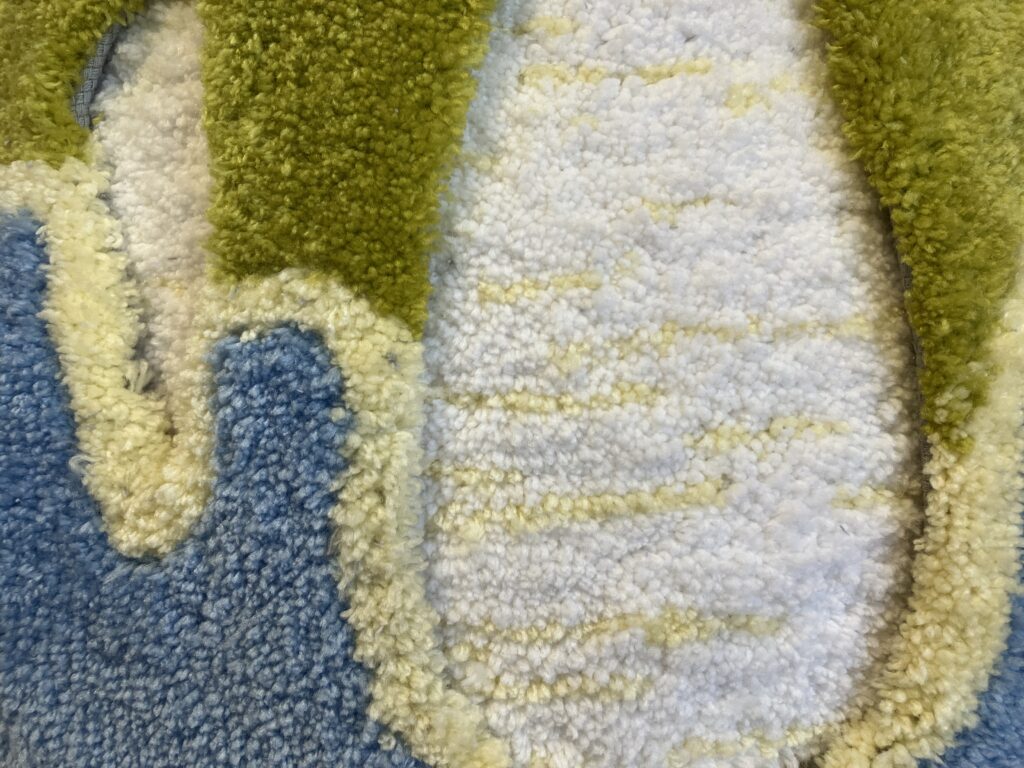 Close-up of rug-like artwork in green, blue, and beige.