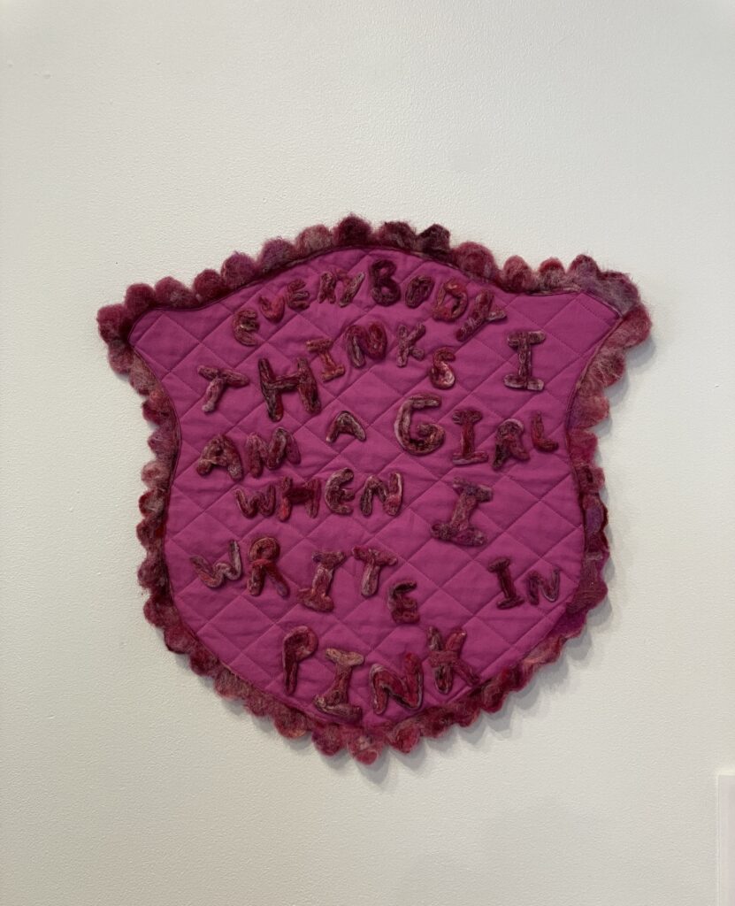 Hot pink felted artwork with darker pink text reading: "Everybody thinks I am a girl when I write in pink"
