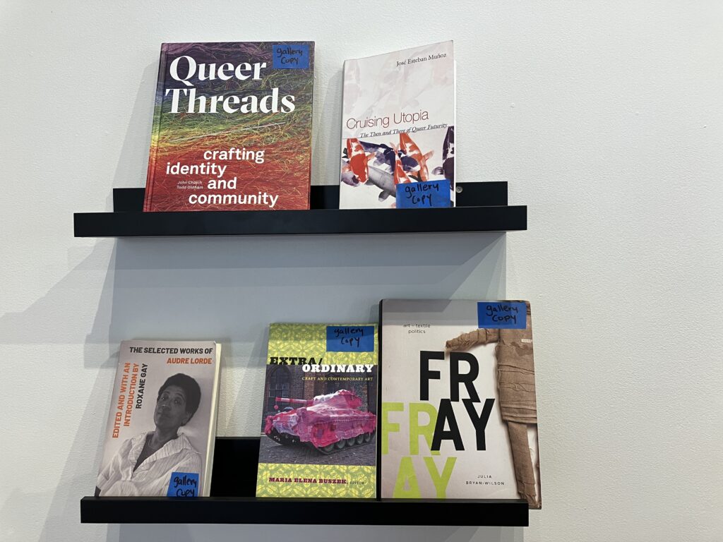 Two shelves with five books displayed, titles include "Queer Threads" and "Fray".