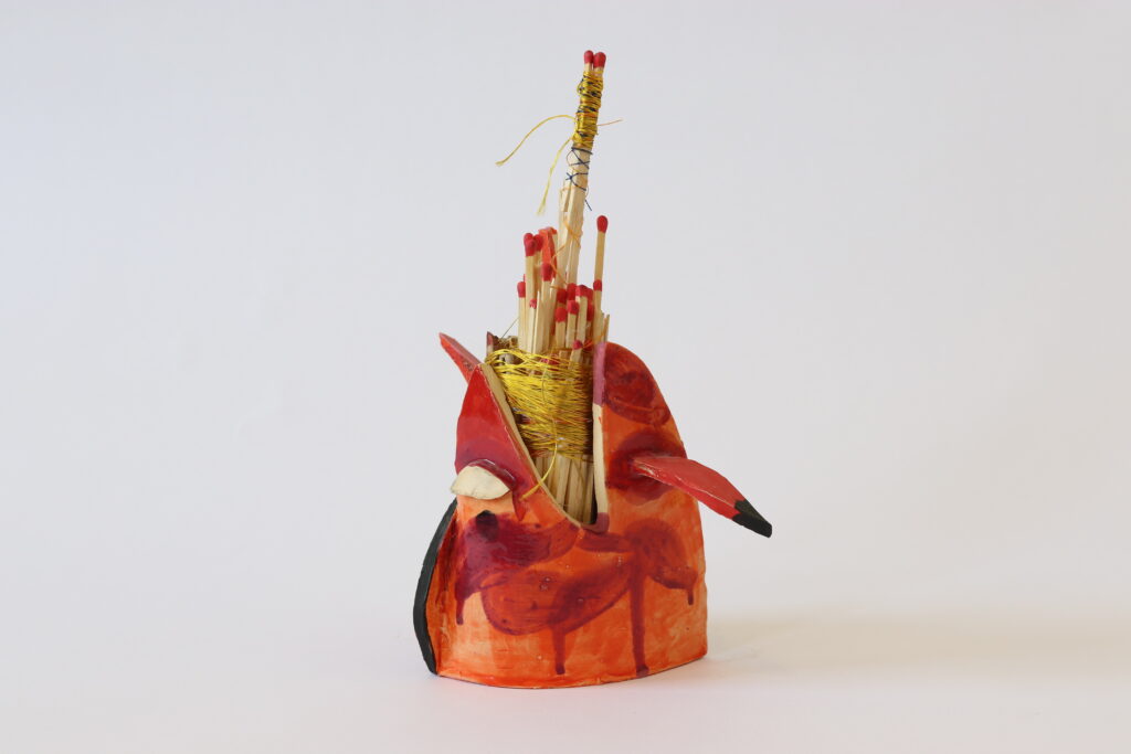 Small sculpture painted red with bunches of matches tied with twine.