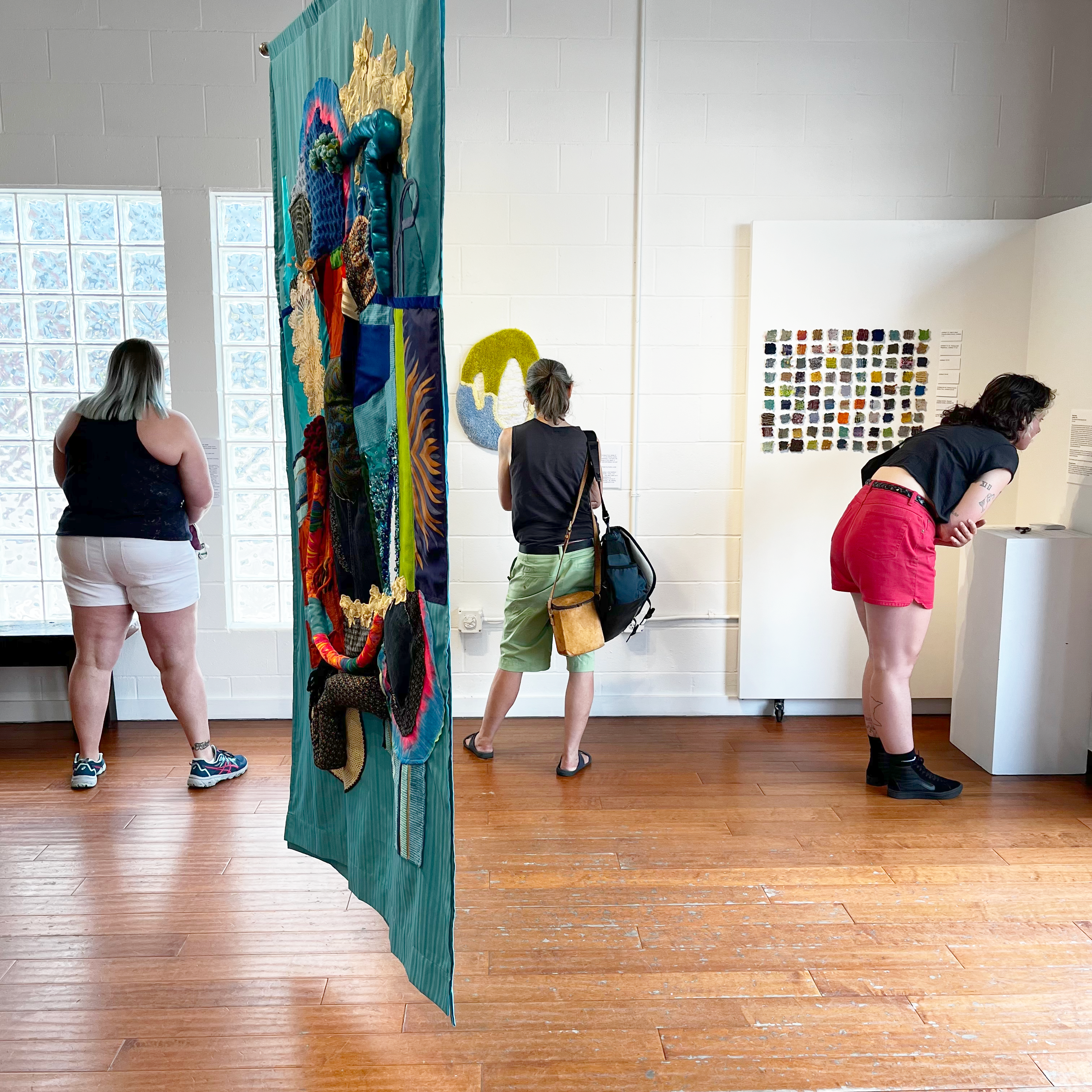 Three people look at art in gallery, with large hanging textile.