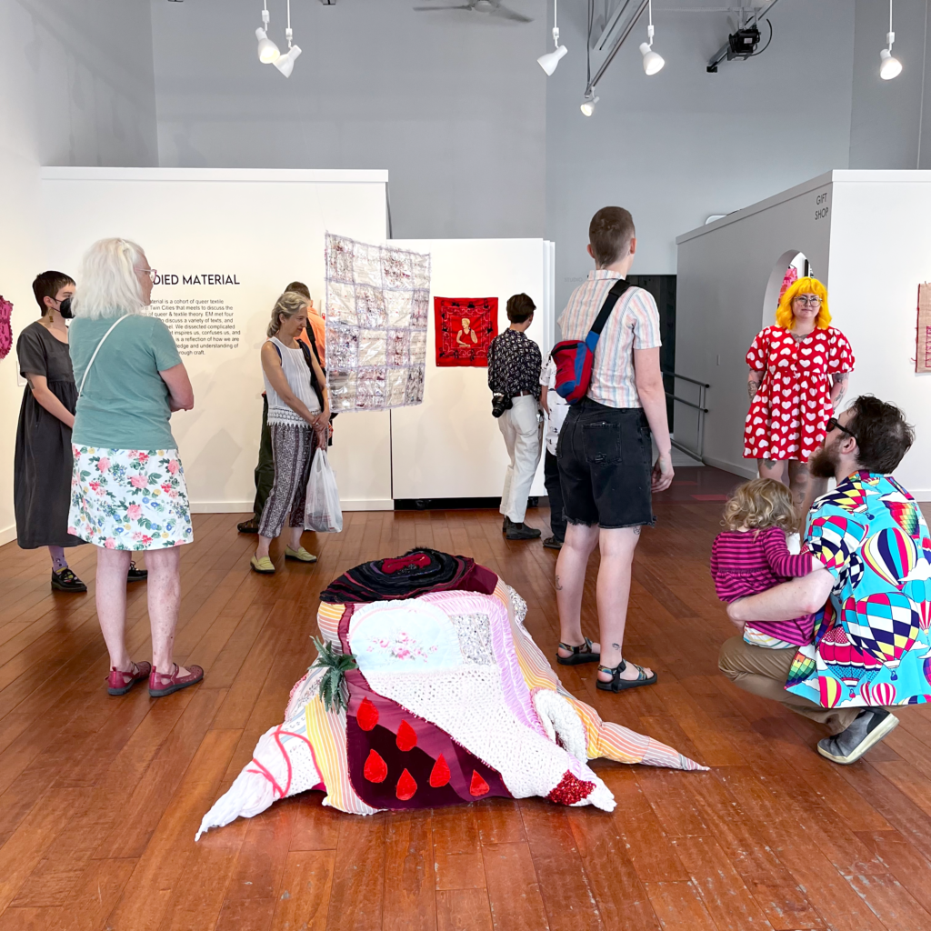 People look at art in gallery, with textile sculpture on floor.