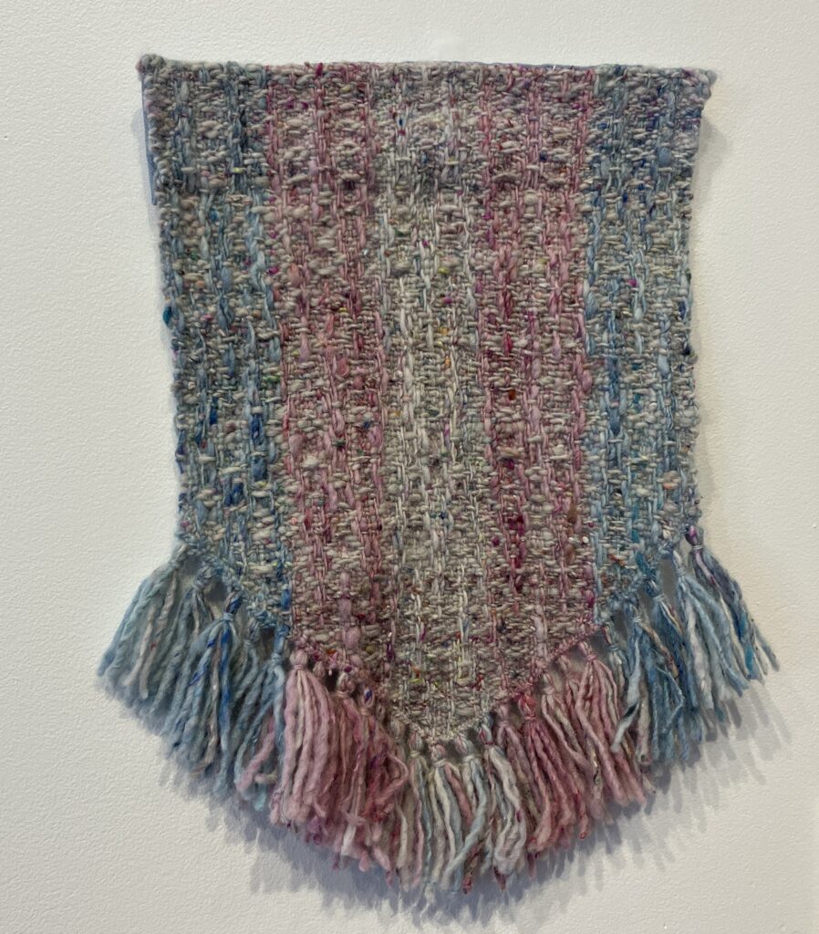 Woven flag in blue, pink, and white stripes hanging on wall.