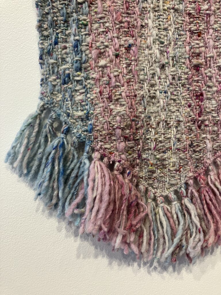 Woven flag in blue, pink, and white stripes hanging on wall.