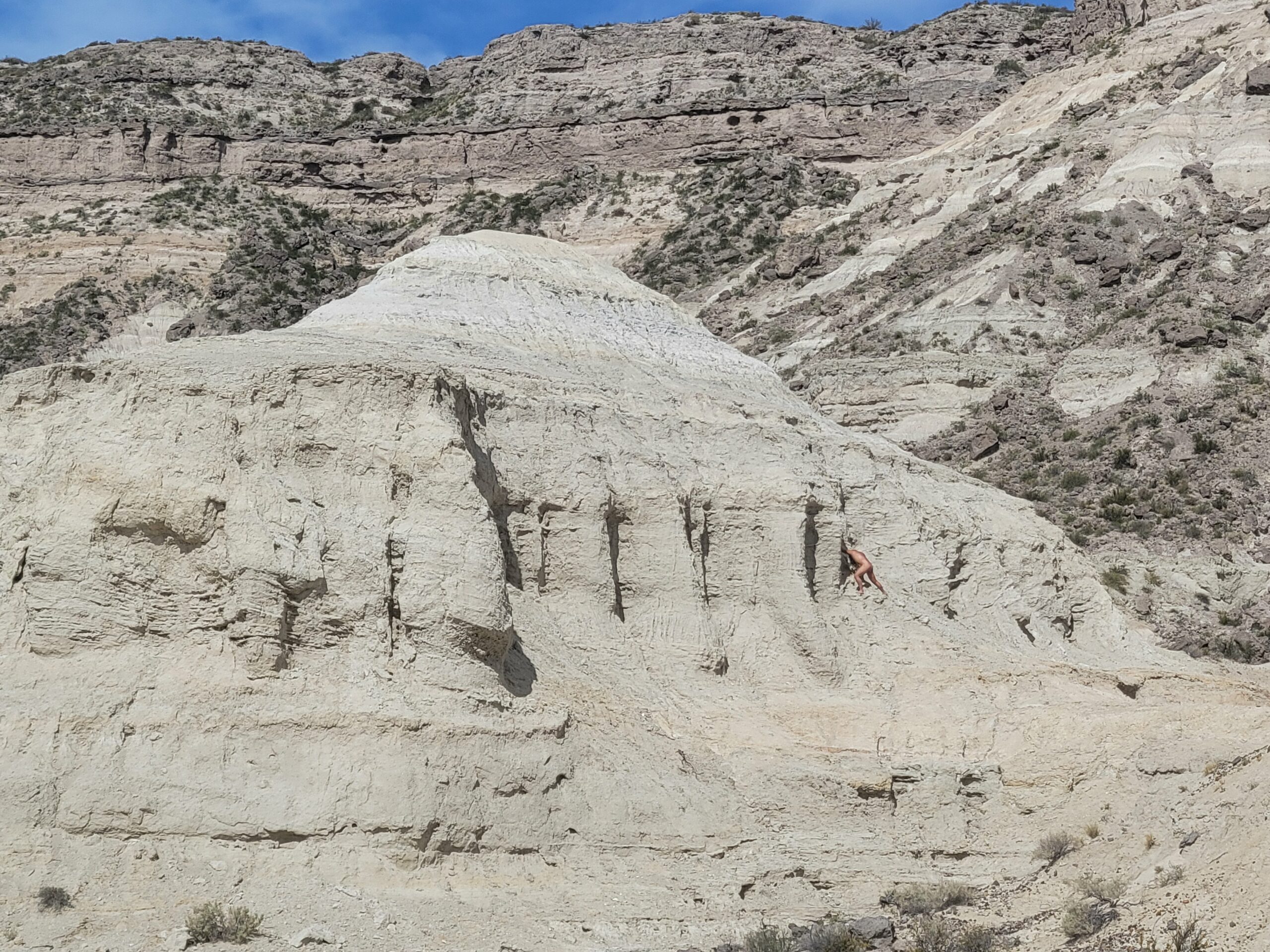 Nude body presses into rock formation in desert landscape.