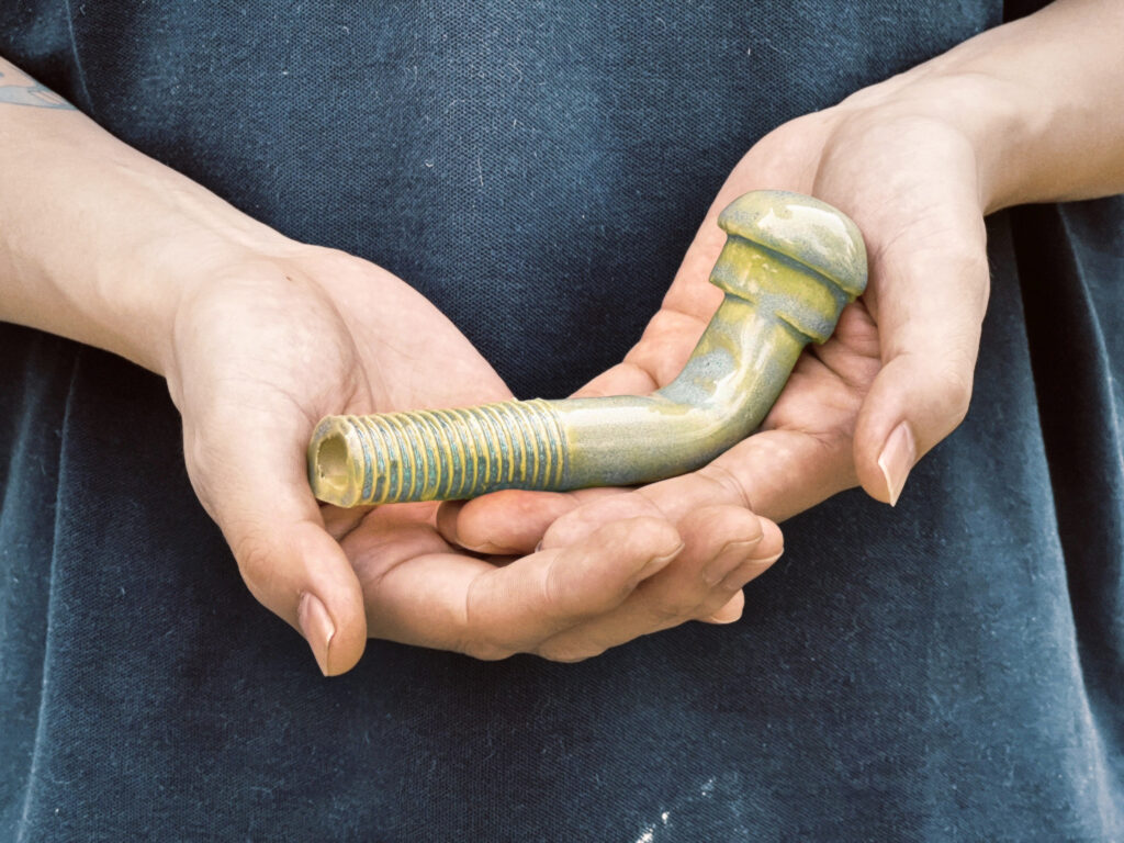 Two hands hold a ceramic scupture shaped like a large bolt, bent near the top.