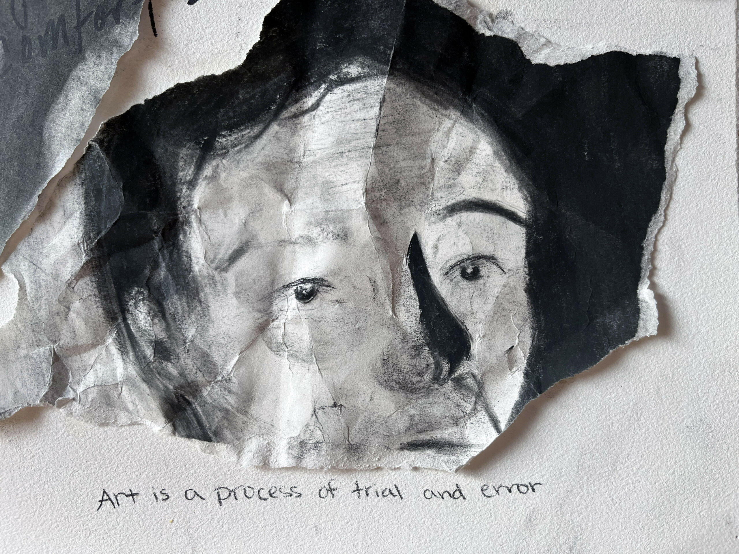 Black and white drawing of a face, torn out and placed on white paper reading: "Art is a process of trial and error."