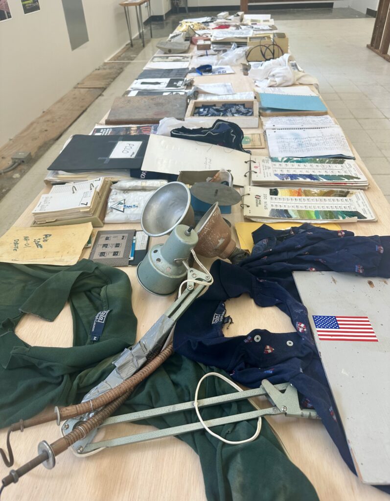 Long table covered with many notebooks, desk lamps, and fabric.