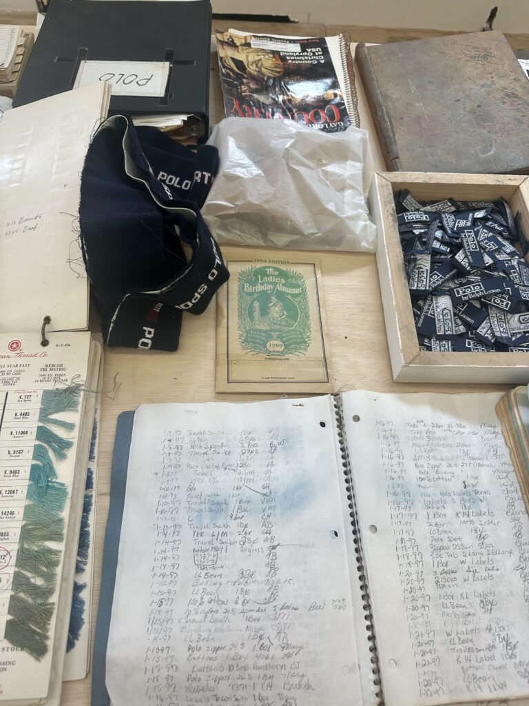 Notebooks, magazine, binders, thread samples, clothing tags, and other items lay on table.