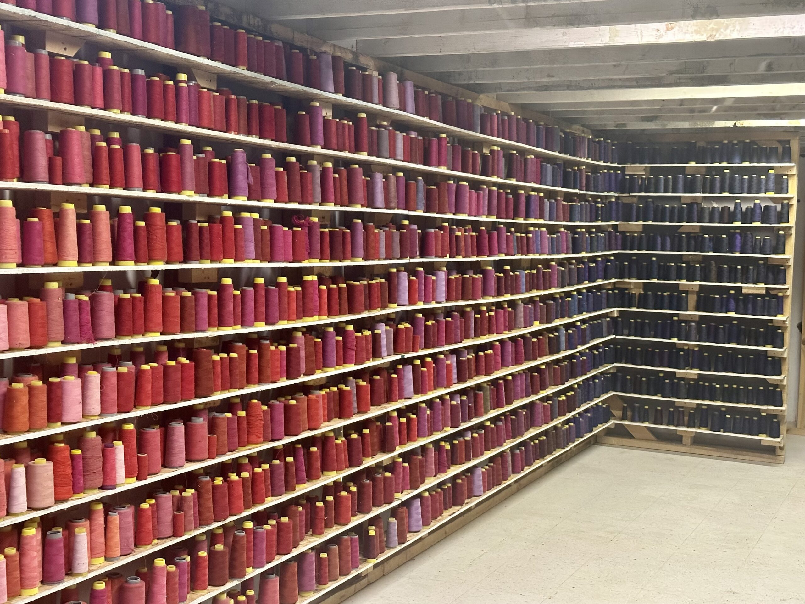 Many spools of red and purple thread on floor-to-ceiling shelving.