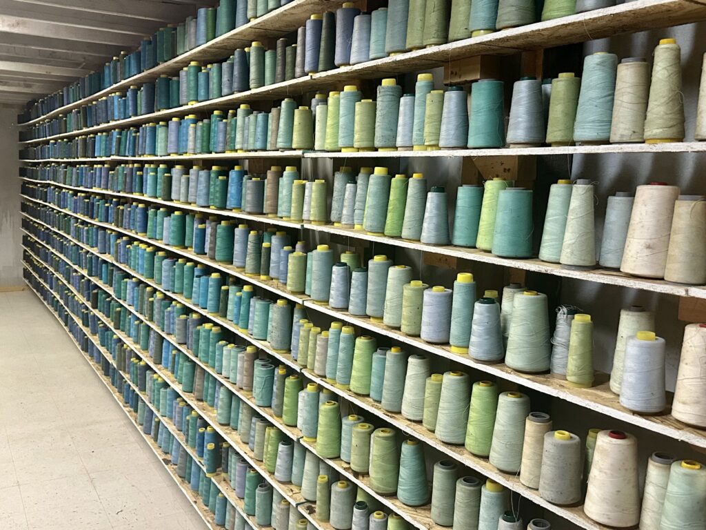 Many spools of blue and green thread on floor-to-ceiling shelving.