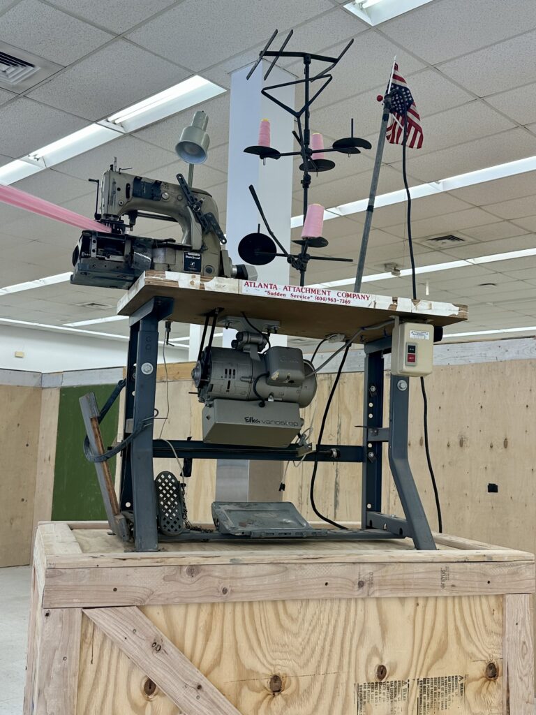 Sculpture with shipping crate, sewing machine, desk lamp, and small American flag.