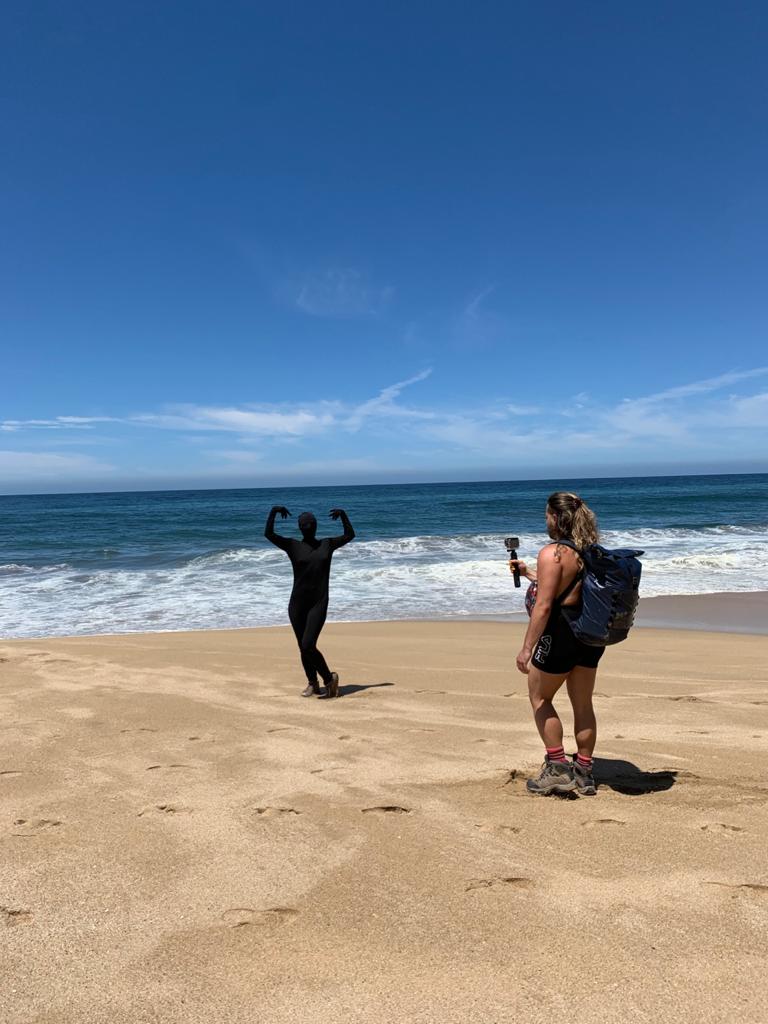 Person takes a photo of another person on ocean beach with blue sky.