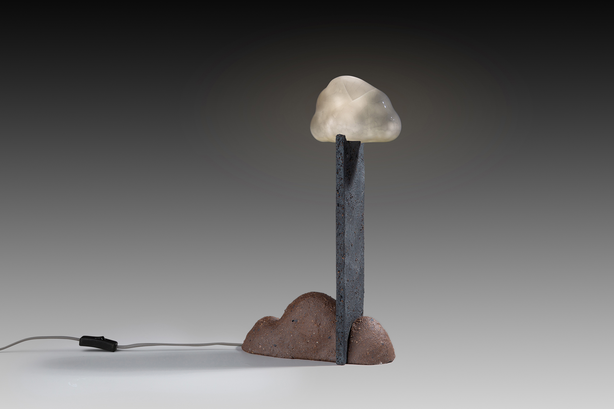 Sculptural lamp with electrical cord, brown cloud-shaped base, flat pillar, and white cloud light.