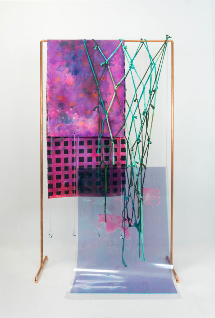 Multimedia artwork with fuschia fabric, teal netting, and lavender plastic sheet draped over copper frame.