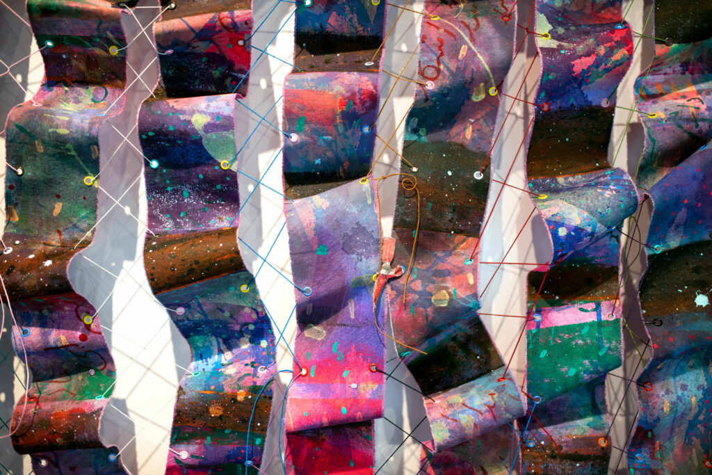 Close-up of multicolored painted canvases woven together with waxed thread and grommets.