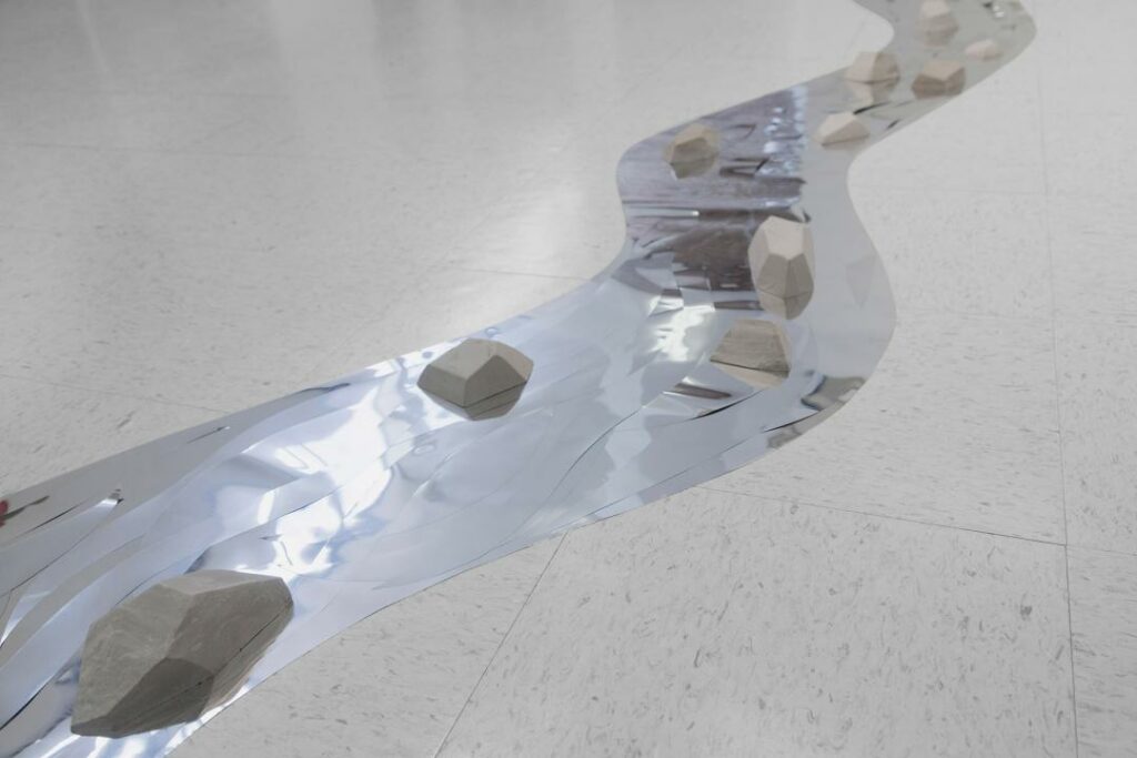 Sculpture with rock forms sitting on strip of silver mylar on white terrazo floor.