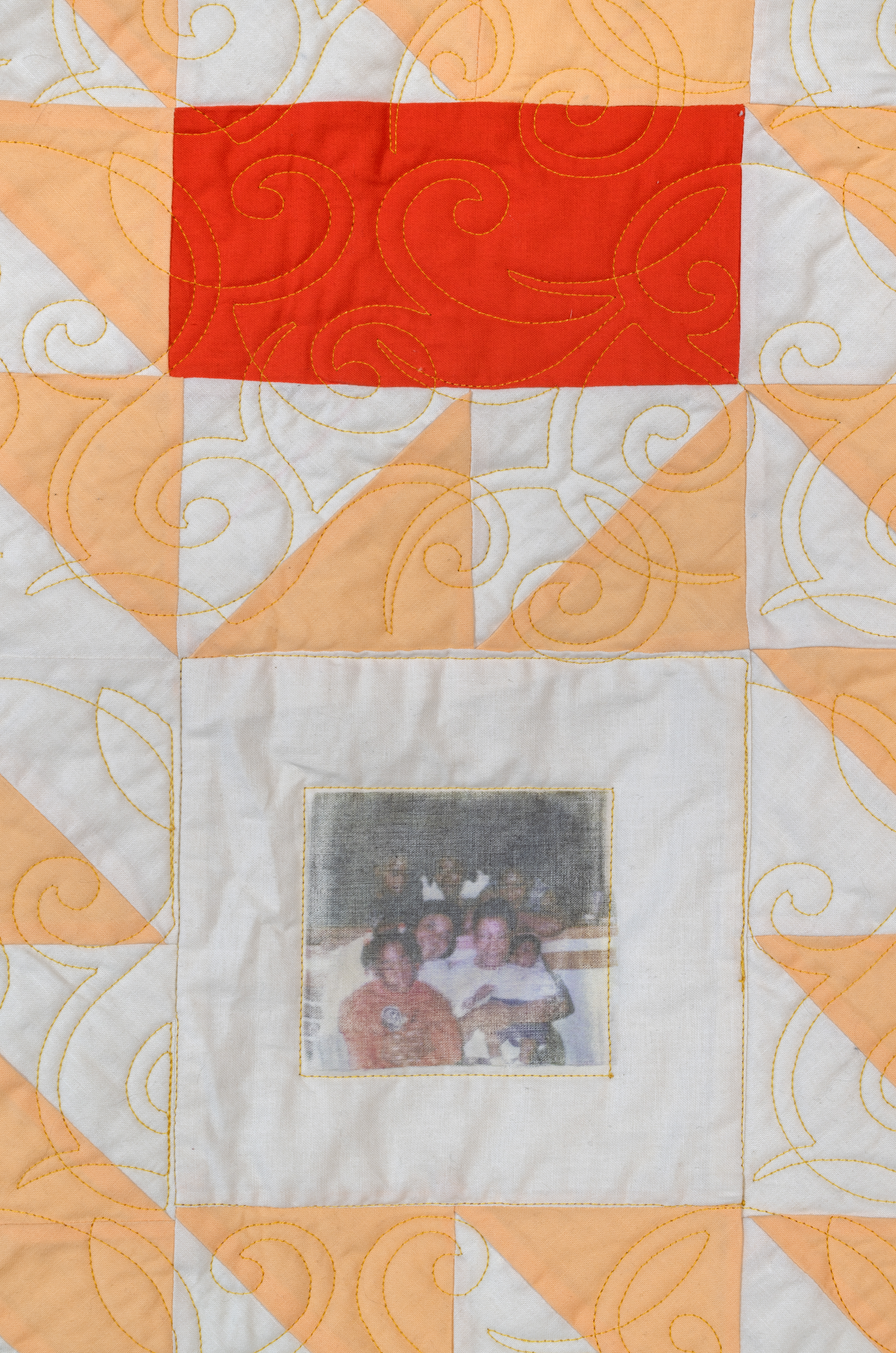 White, peach, and red quilt with family photograph in center.
