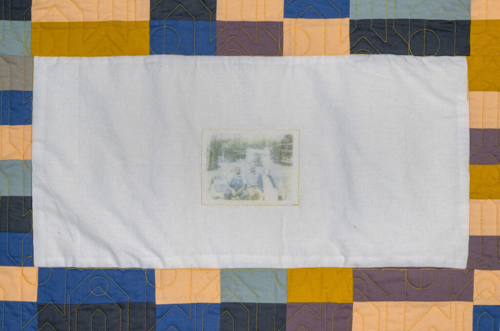 Detail of quilt with vintage photograph on white fabric, surrounded by blue and brown pattern.