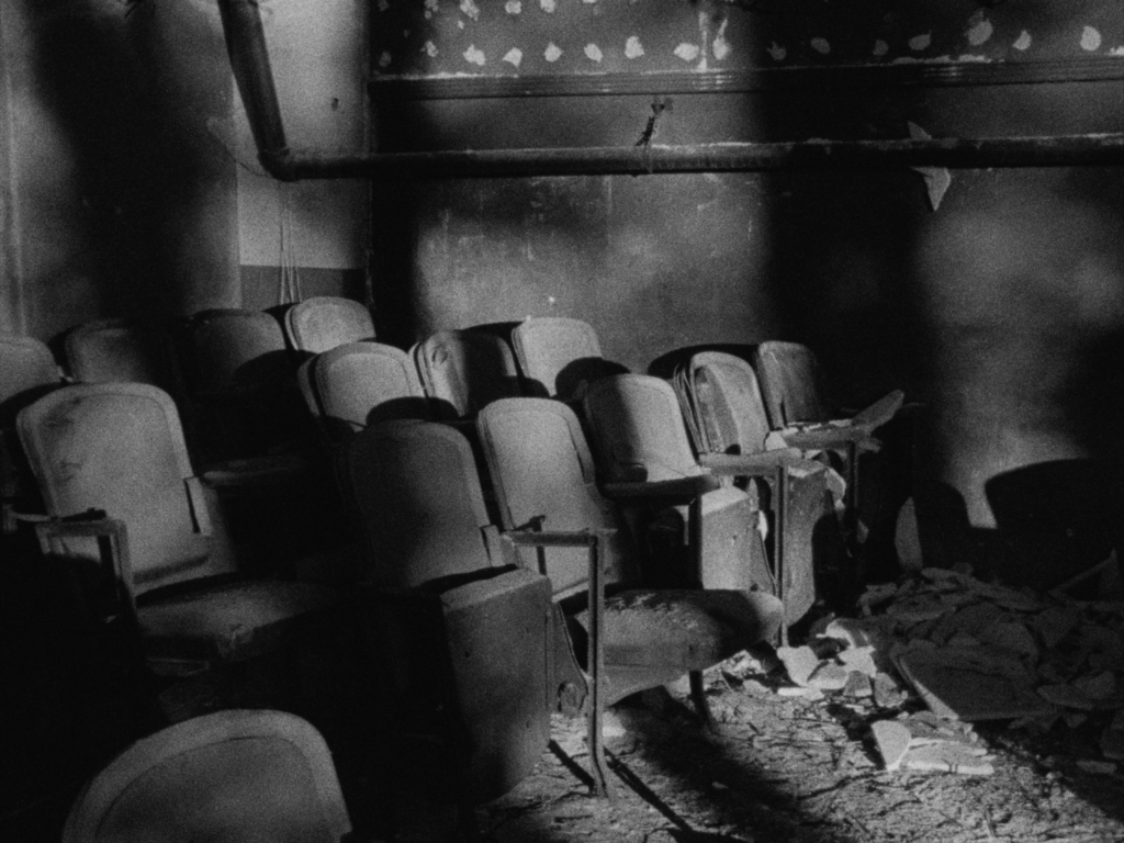 Black and white film still of abandoned theater seats in shadow.