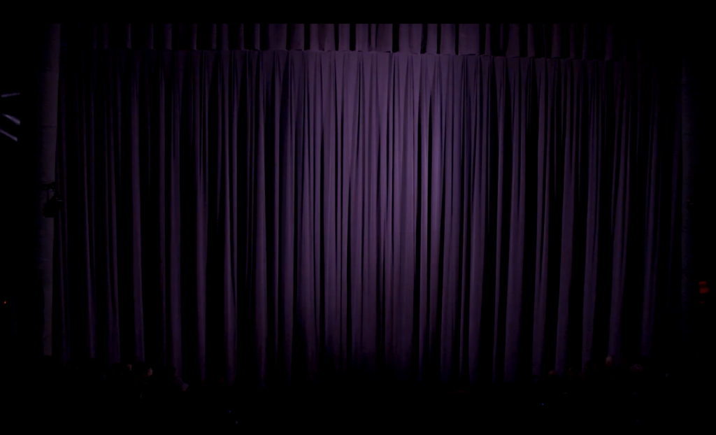 Low light on closed purple theater curtain.