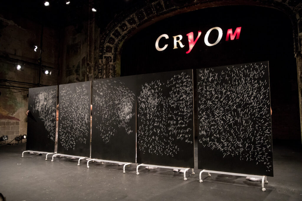 Stage with arch and five chalkboards on wheels, covered with repetitive shapes in white chalk.