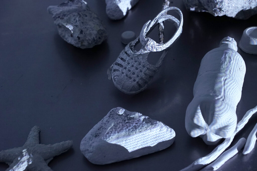 Cast concrete and metal objects under blue-grey light: a child's shoe, pop bottle, rocks