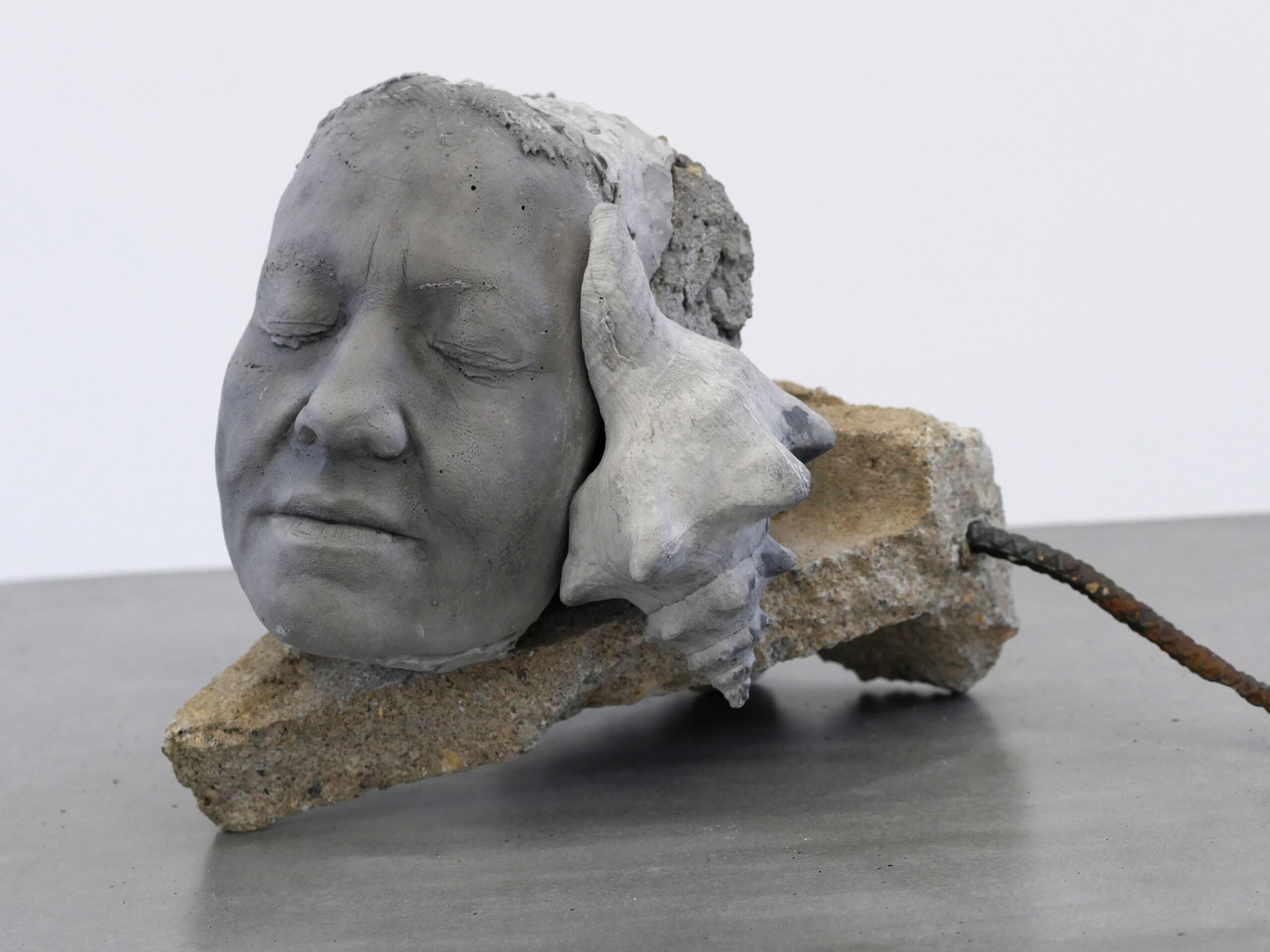 Cast concrete face with closed eyes and seashell mounted on concrete shard
