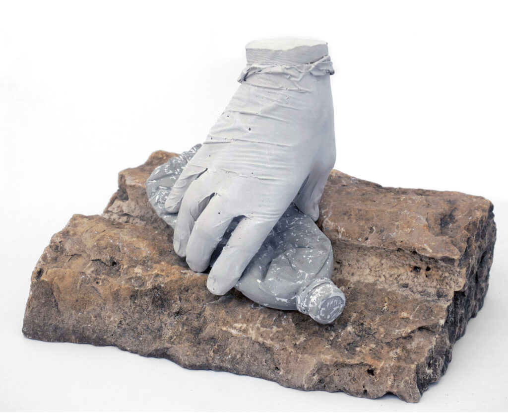 Gloved hand picking up plastic bottle in cast concrete mounted on rock