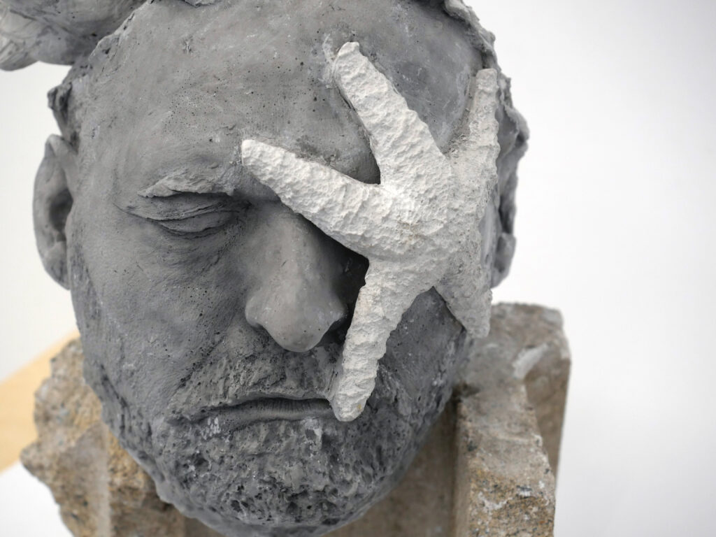 Face with closed eyes and beard and star fish across one eye cast in concrete