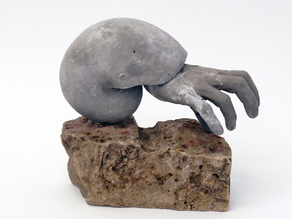 Hand emerging from shell cast in concrete and mounted on stone