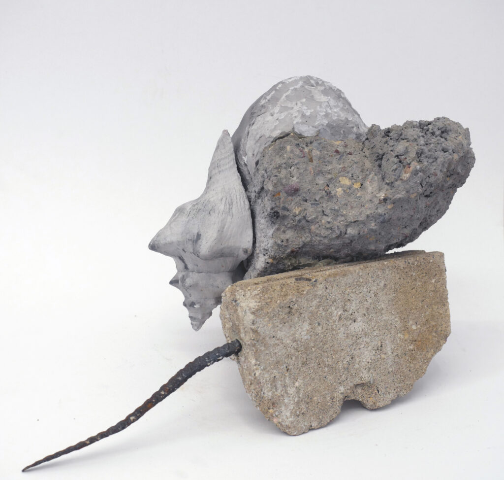 Shard of concrete with iron poking out, with shell of cast concrete mounted on top