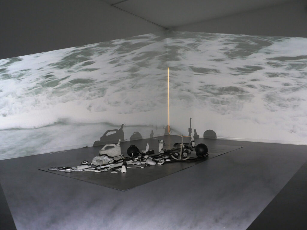 Cast concrete objects spread across floor with projection of ocean on walls and floor
