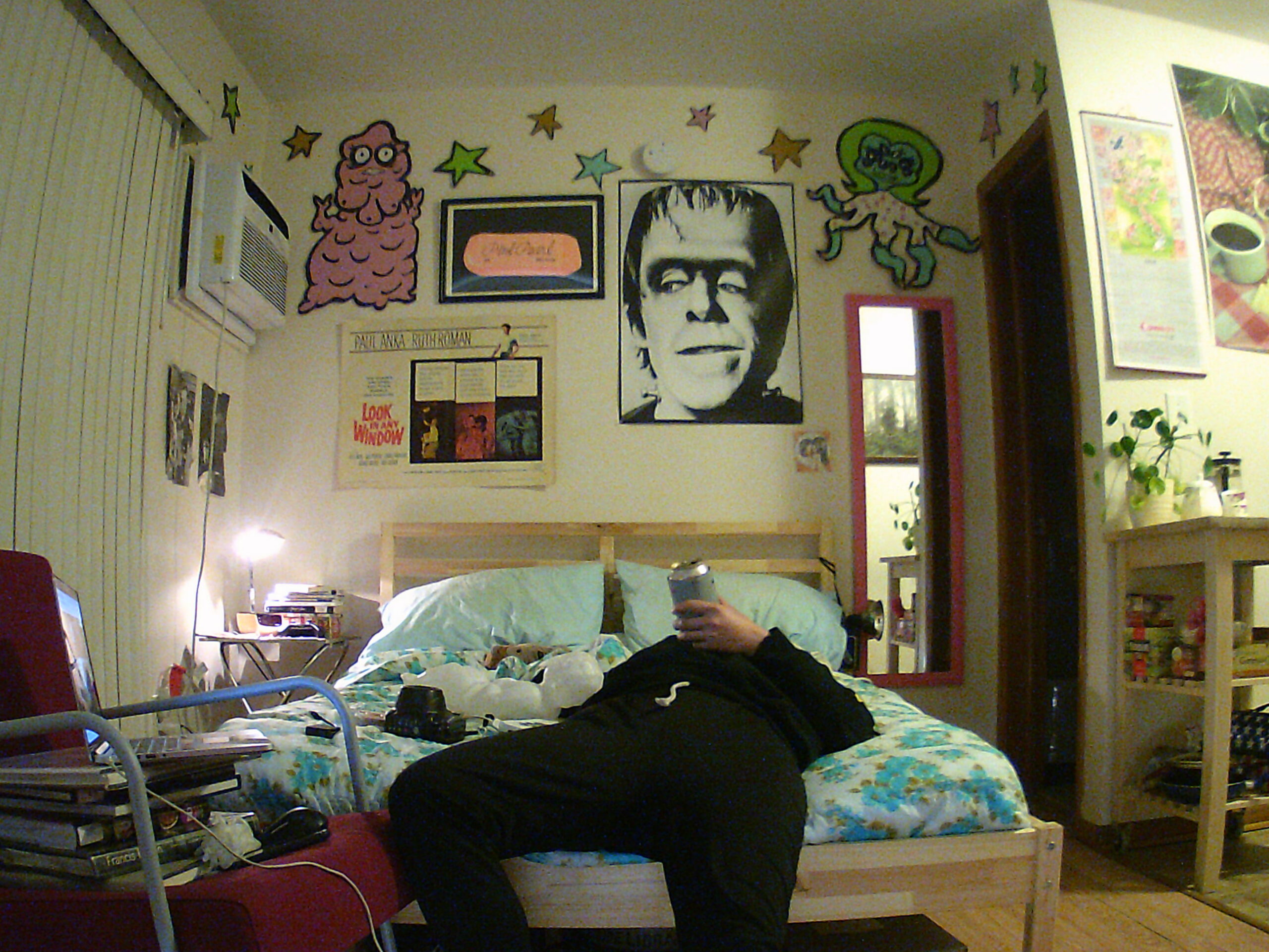 Person laying back on bed in bedroom with cartoons and art on walls