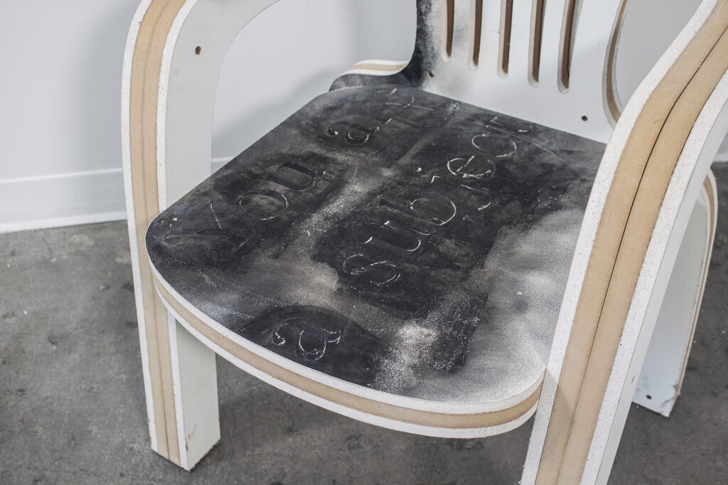 Chair made of MDF and drywall with "you are a subject" written amidst black on seat