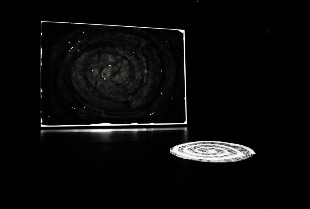 Black space with a dark screen and faint dark spiral, and a light white spiral on the floor.