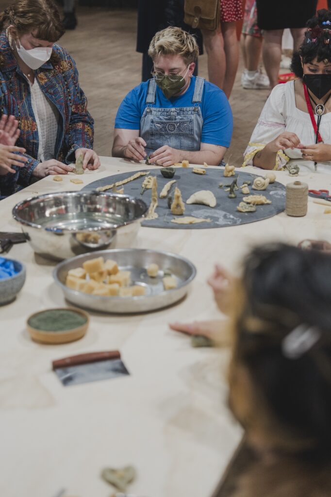 Masked participants are seated on the floor, molding objects by hand.