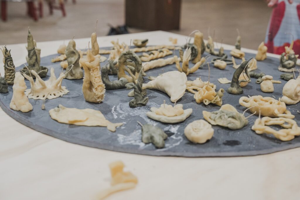 Small objects in various forms made of beeswax arranged on a round grey stone.