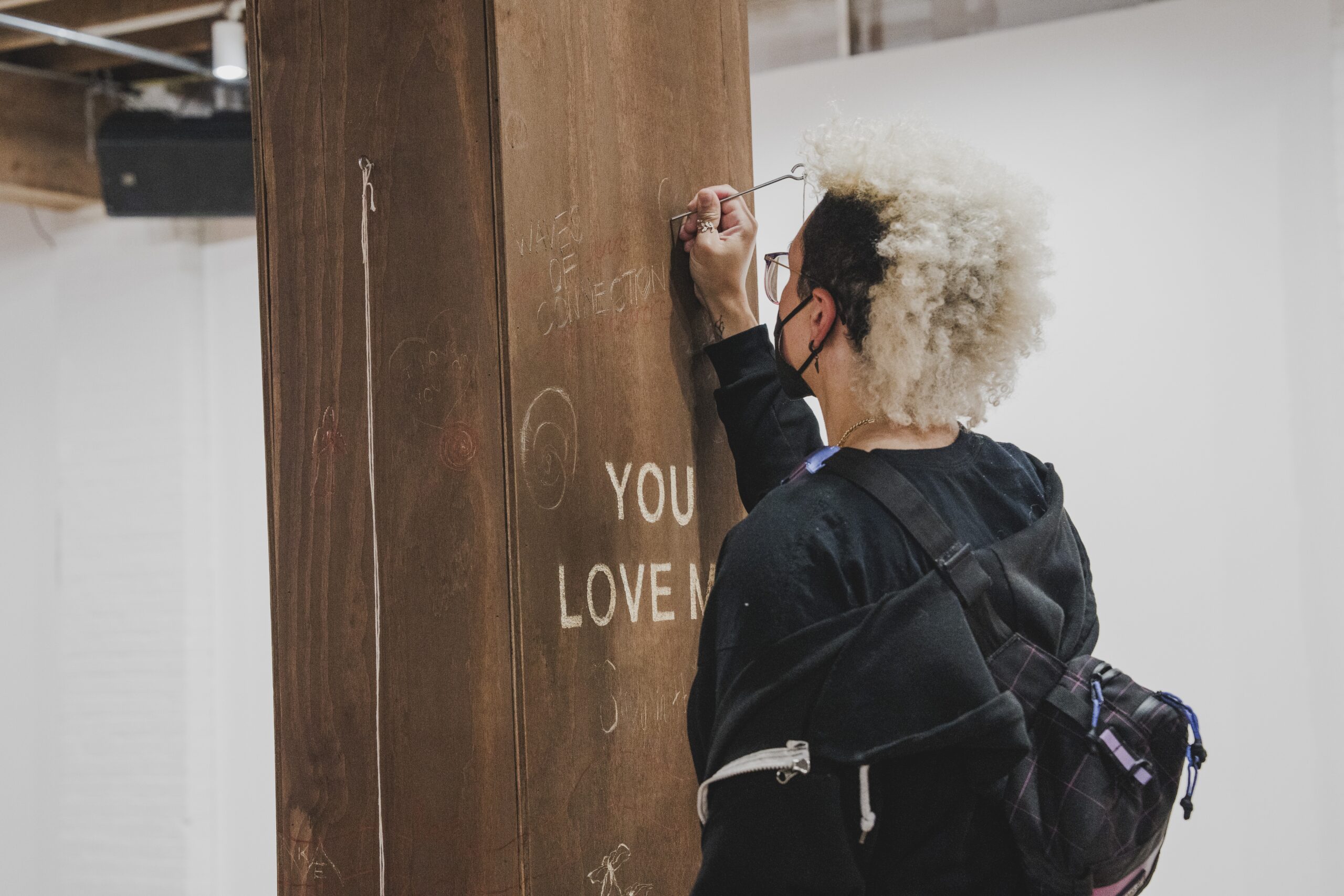 Person stands in front of wooden post using metal tool to inscribe in it.