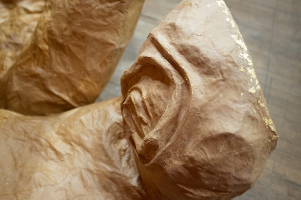 Close up of a brown paper mache sculpture of a ridged finger, belonging to a larger hand.